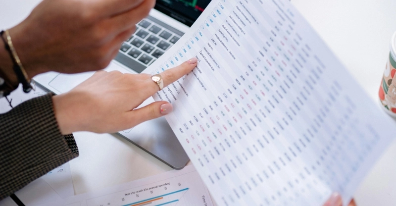 A person points at a document on a table, indicating its importance or relevance in the discussion