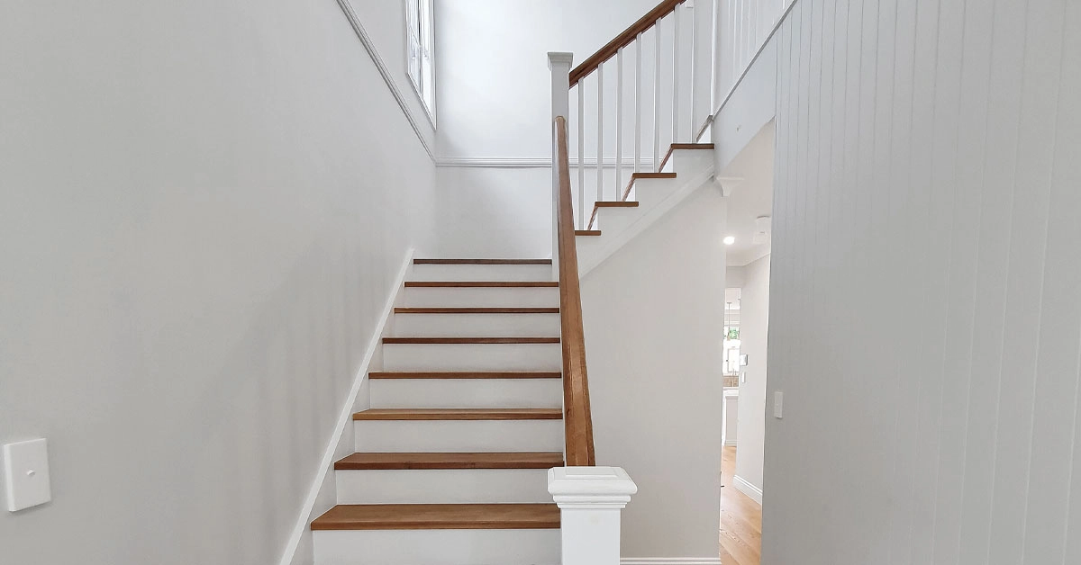Modern staircase with light wood steps and white railings in a bright, minimalistic interior. Soft natural light illuminates the space, conveying tranquility.