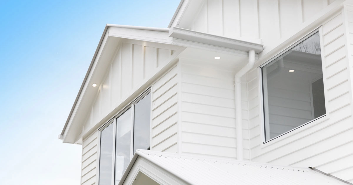 Modern white house exterior with vertical siding, large windows, and gabled roof. The blue sky adds a serene backdrop to the sleek, clean design.