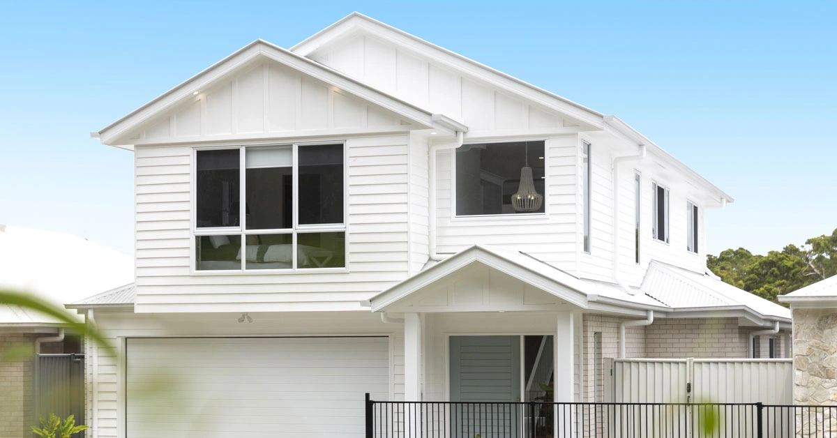 Modern two-story white house with large windows, a double garage, and a small front yard enclosed by a black fence. Bright and inviting.